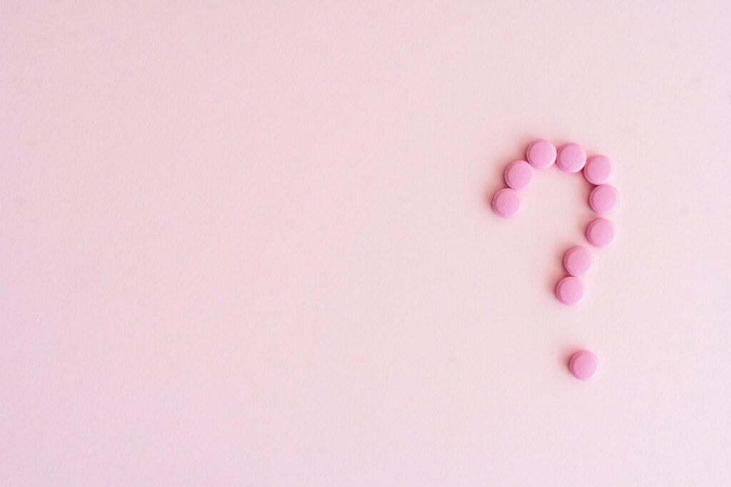 A question mark created from pink pills on a light pink surface, symbolizing uncertainty in health decisions.